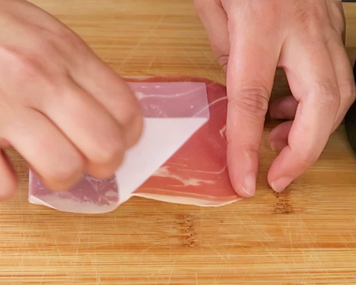 peeling the wax off a piece of prosciutto on a cutting board